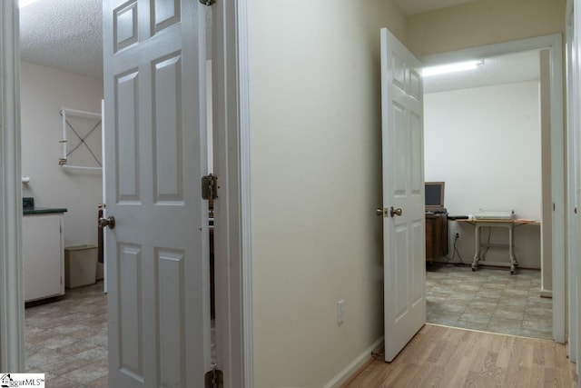 hall featuring a desk, light wood-type flooring, and a textured ceiling