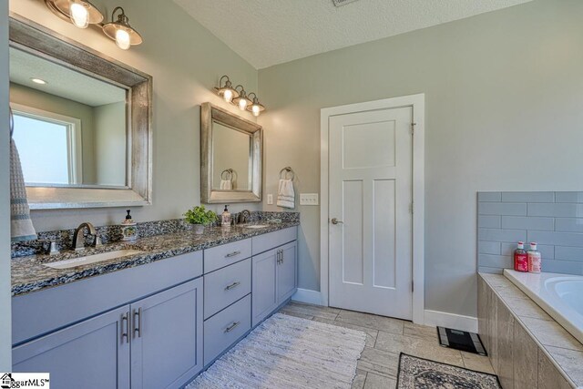 2007 Edwards Lake Rd, Greer, SC 29651 - bathroom with baseboards, double vanity, tiled bath, and a textured ceiling