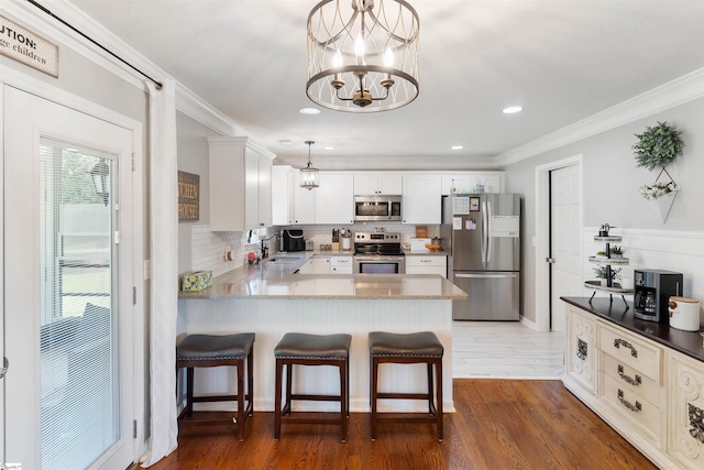 kitchen with appliances with stainless steel finishes, a chandelier, backsplash, a peninsula, and crown molding