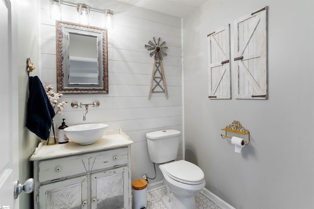 half bathroom featuring toilet, vanity, wooden walls, and baseboards
