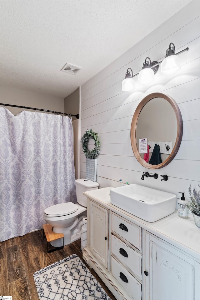 bathroom featuring a textured ceiling, wood finished floors, vanity, toilet, and wooden walls
