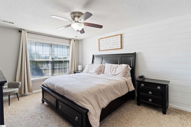 bedroom with a textured ceiling, light colored carpet, baseboards, ceiling fan, and wooden walls