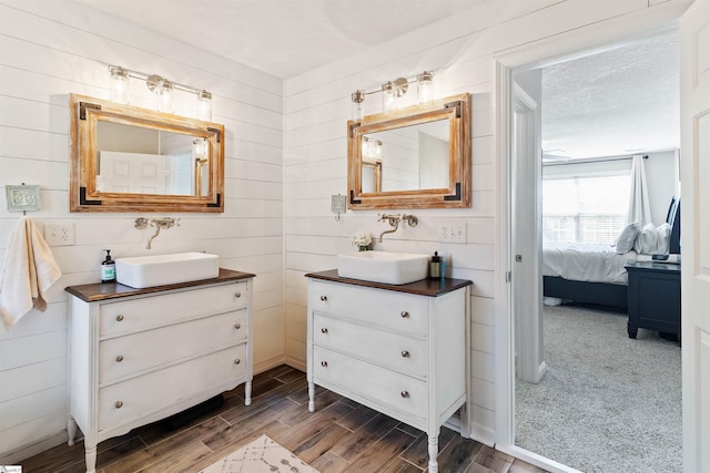 ensuite bathroom with wood finished floors, two vanities, and wooden walls