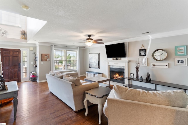 living room featuring wood finished floors, a textured ceiling, a fireplace with flush hearth, ceiling fan, and ornamental molding