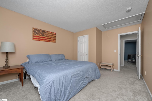 bedroom with attic access, light colored carpet, baseboards, and a textured ceiling