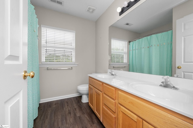 bathroom featuring baseboards, wood finished floors, toilet, and double vanity
