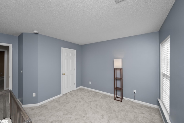 carpeted empty room featuring a textured ceiling, baseboards, and a smoke detector