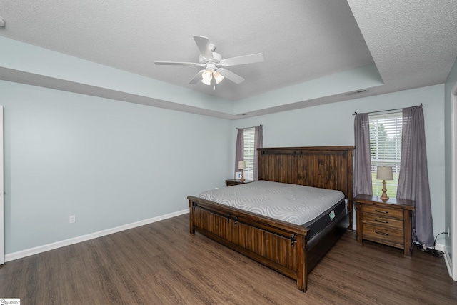 bedroom with wood finished floors, a textured ceiling, baseboards, ceiling fan, and a raised ceiling