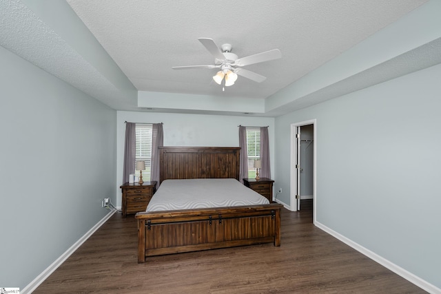bedroom with baseboards, wood finished floors, ceiling fan, a walk in closet, and a textured ceiling