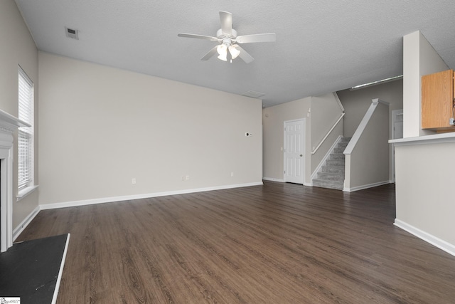 unfurnished living room with a ceiling fan, dark wood finished floors, stairway, baseboards, and a textured ceiling