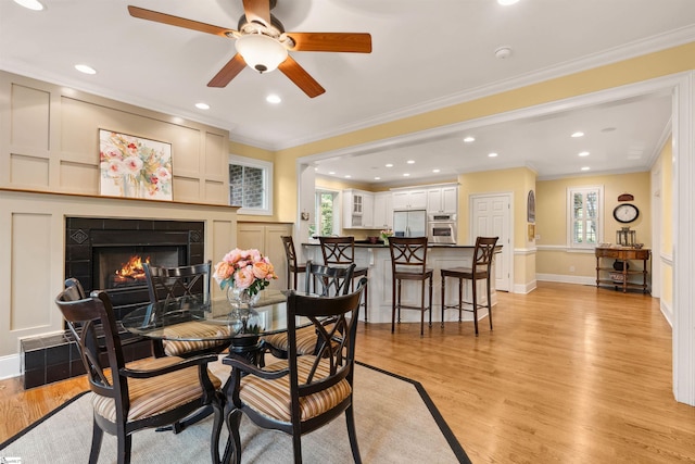 201 King Eider Way, Taylors, SC 29687 - dining space with a warm lit fireplace, light wood-type flooring, a ceiling fan, baseboards, and ornamental molding