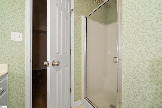full bathroom with wallpapered walls, a stall shower, and vanity