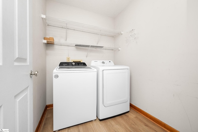laundry room featuring light wood finished floors, washer and dryer, and baseboards