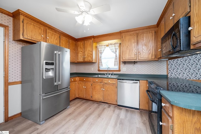 kitchen with black appliances, a sink, light wood-style floors, brown cabinetry, and wallpapered walls