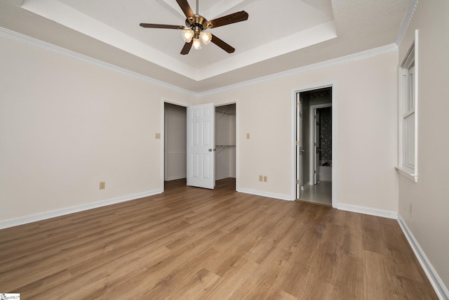 unfurnished bedroom featuring a tray ceiling, light wood-type flooring, baseboards, and ornamental molding