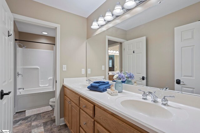 bathroom with double vanity, shower / tub combination, stone finish floors, and toilet
