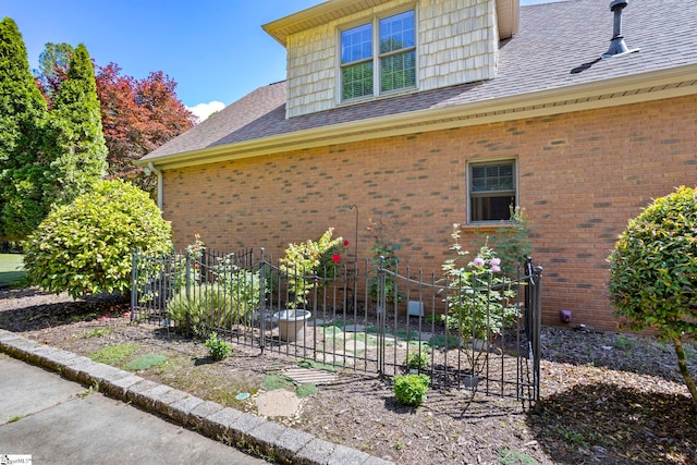 view of home's exterior with fence, roof with shingles, and brick siding