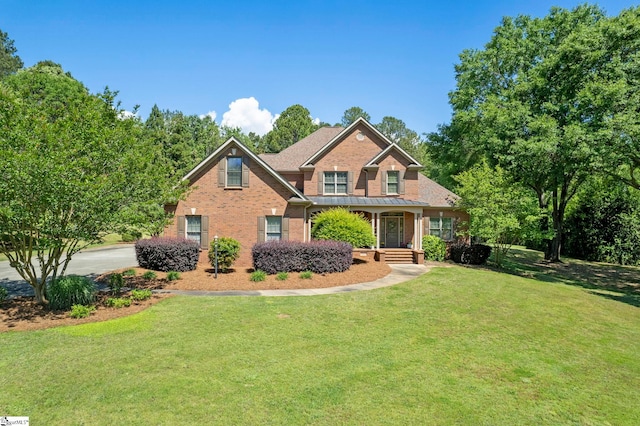 traditional-style house featuring a porch, brick siding, a front lawn, and a standing seam roof