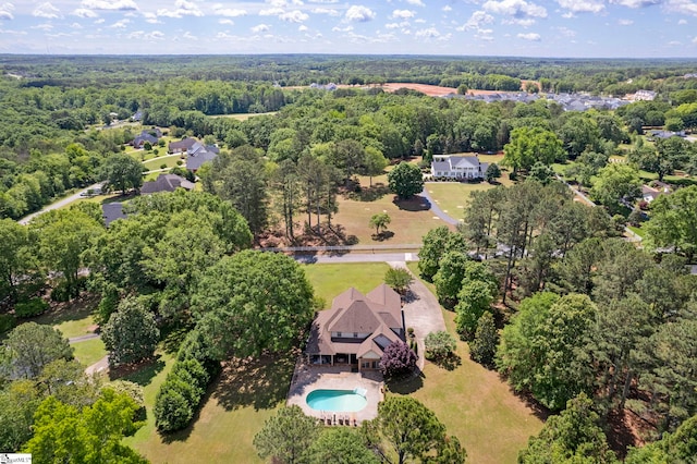 aerial view of property and surrounding area featuring a pool area and a heavily wooded area