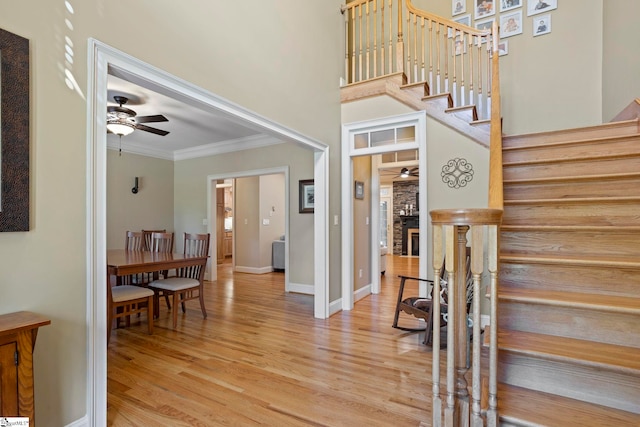stairs featuring a ceiling fan, wood finished floors, ornamental molding, baseboards, and a high ceiling