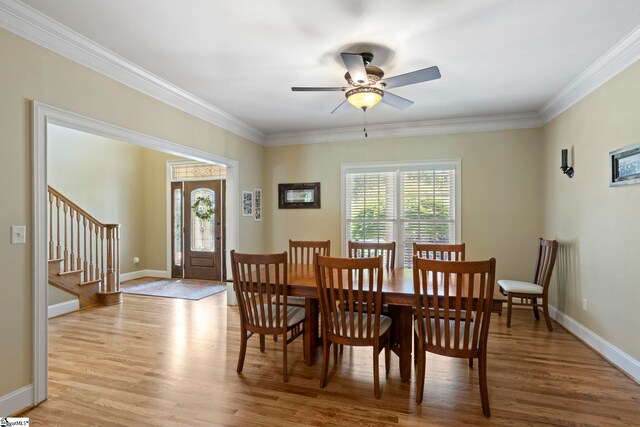 dining space featuring light wood-style floors, crown molding, stairway, baseboards, and ceiling fan