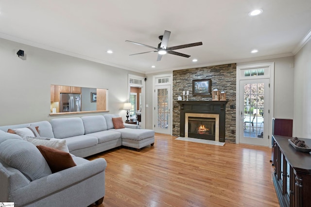 living area featuring ceiling fan, crown molding, light wood-type flooring, recessed lighting, and a stone fireplace