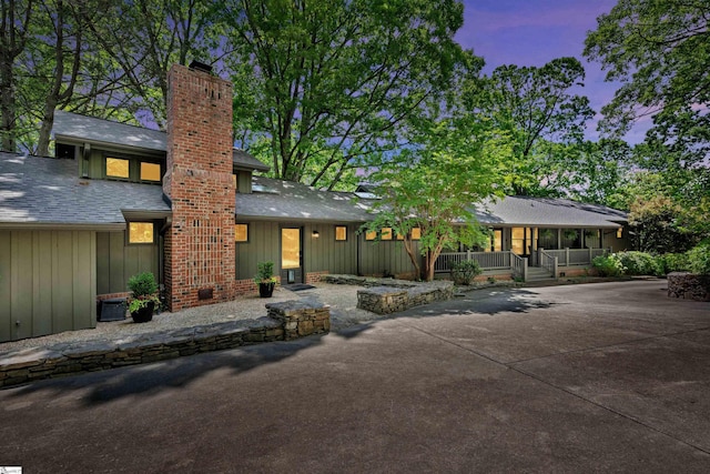 back of property at dusk featuring board and batten siding, a chimney, a porch, and roof with shingles