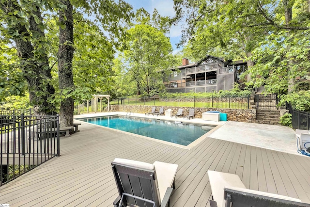 view of pool with a deck, fence, and view of wooded area