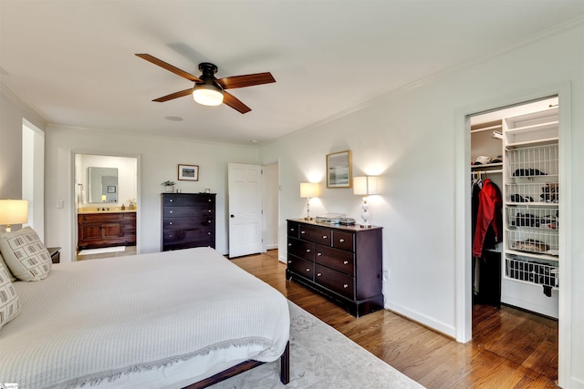 bedroom with a spacious closet, wood finished floors, crown molding, a closet, and a ceiling fan
