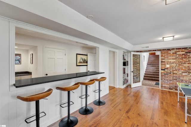 indoor dry bar featuring stairs, wood finished floors, built in shelves, brick wall, and baseboards