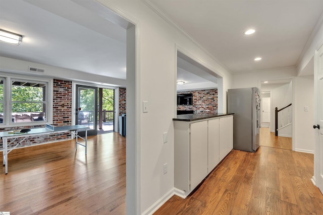 hall with light wood-type flooring, crown molding, baseboards, recessed lighting, and brick wall