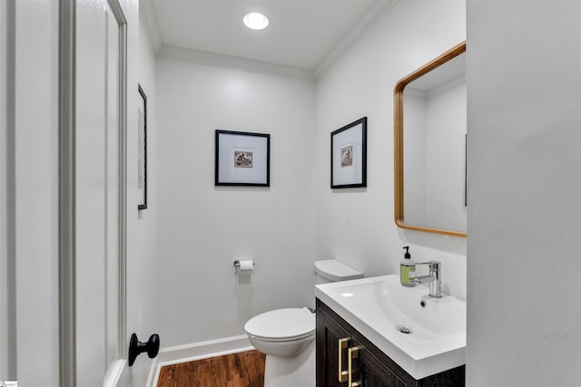 bathroom with toilet, wood finished floors, vanity, baseboards, and crown molding