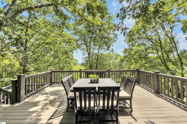 deck with outdoor dining area and view of wooded area