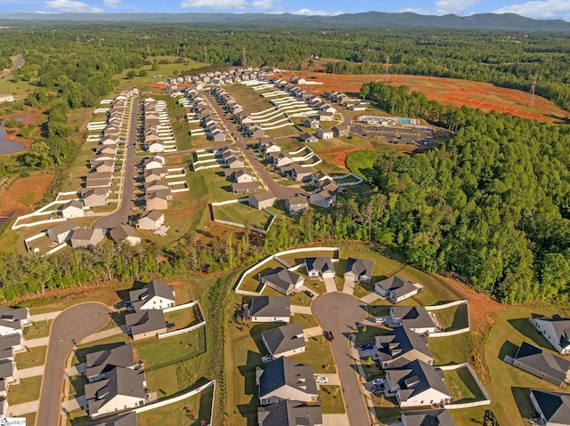 aerial overview of property's location with a forest, nearby suburban area, and a mountainous background