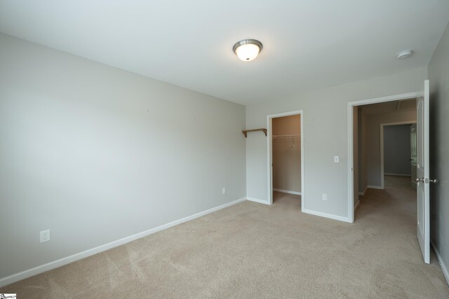 unfurnished bedroom featuring light colored carpet, baseboards, a walk in closet, and a closet