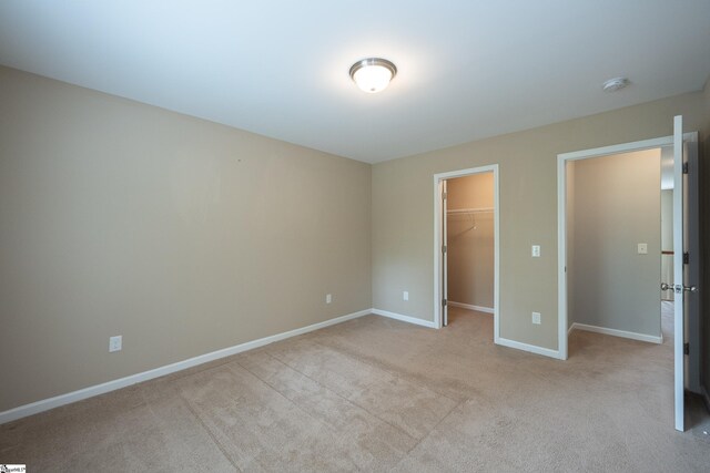 unfurnished bedroom with a spacious closet, light carpet, baseboards, and a closet