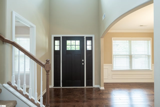 entrance foyer featuring arched walkways, wood finished floors, ornamental molding, a wainscoted wall, and stairway