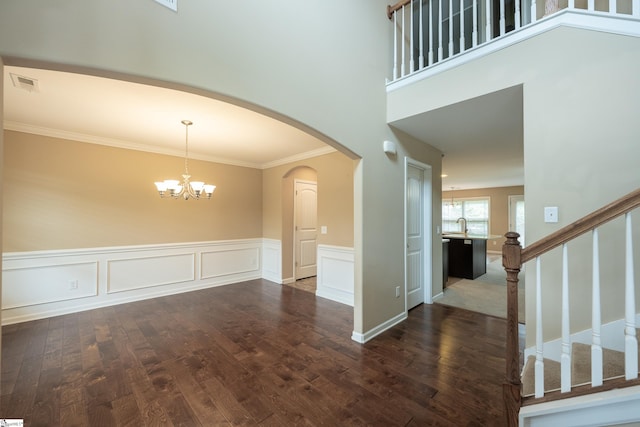 entryway with dark wood-type flooring, a chandelier, crown molding, a wainscoted wall, and stairway