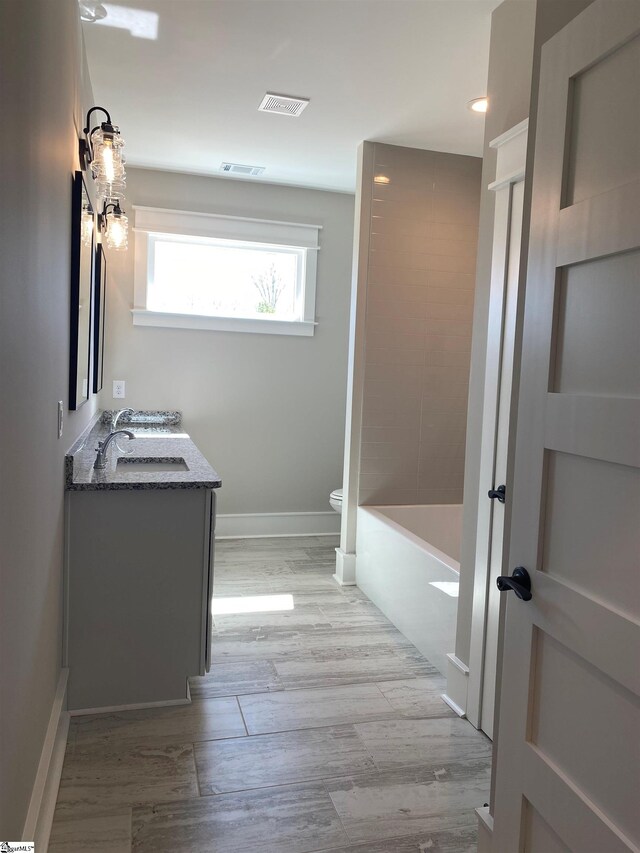 bathroom with toilet, wood finished floors, vanity, baseboards, and recessed lighting