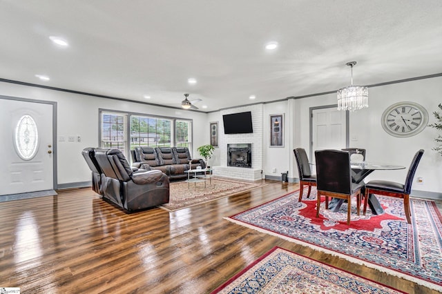 living room with crown molding, ceiling fan, a fireplace, baseboards, and wood finished floors