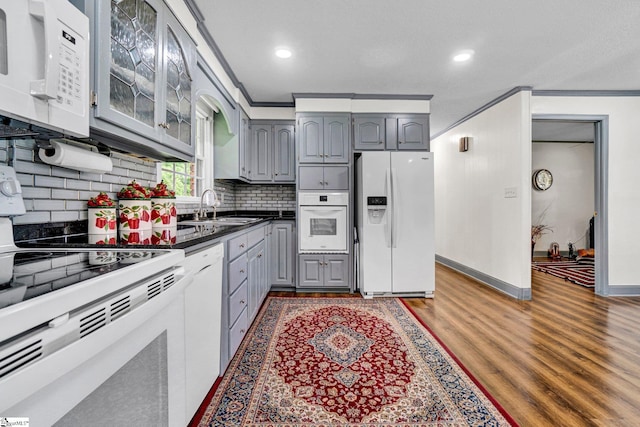 kitchen featuring white appliances, gray cabinetry, a sink, dark countertops, and tasteful backsplash