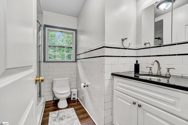 bathroom with tile walls, toilet, wood finished floors, vanity, and wainscoting