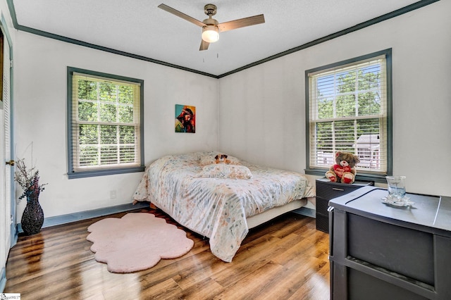 bedroom with ornamental molding, multiple windows, wood finished floors, and ceiling fan