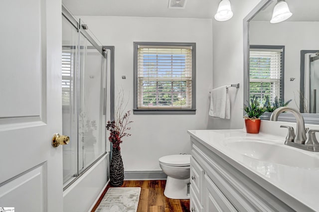 bathroom featuring wood finished floors, toilet, vanity, shower / bath combination with glass door, and baseboards