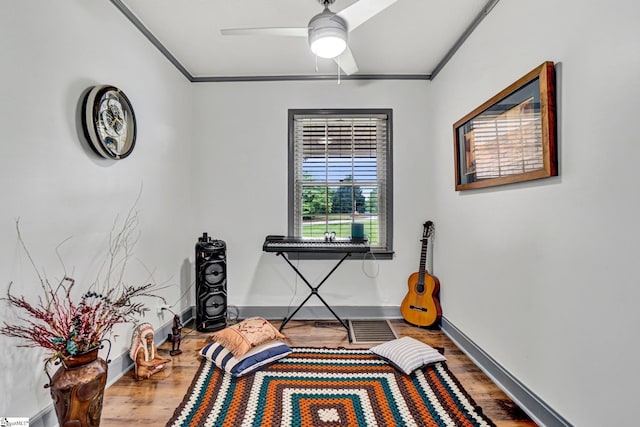 sitting room with wood finished floors, ornamental molding, ceiling fan, and baseboards