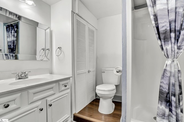 bathroom with a closet, wood finished floors, toilet, vanity, and a shower