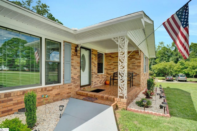 entrance to property featuring covered porch, a yard, and brick siding