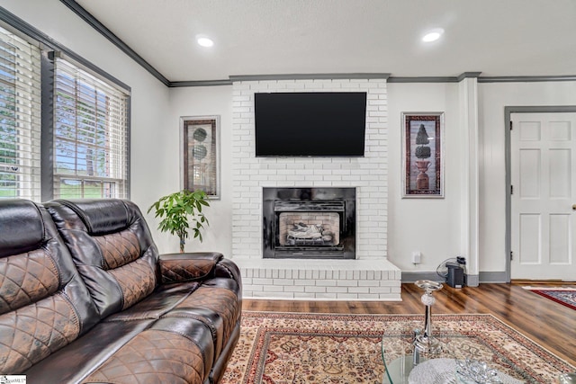 living area featuring ornamental molding, wood finished floors, a brick fireplace, recessed lighting, and baseboards