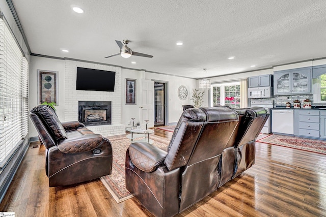 living room with ceiling fan, a textured ceiling, wood finished floors, a brick fireplace, and healthy amount of natural light