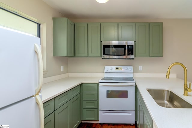kitchen with white appliances, green cabinetry, a sink, and light countertops
